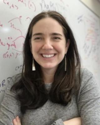white woman with brown hair and dangling earrings standing in front of whiteboard